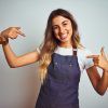 Young beautiful woman wearing apron over grey isolated background looking confident with smile on face, pointing oneself with fingers proud and happy.